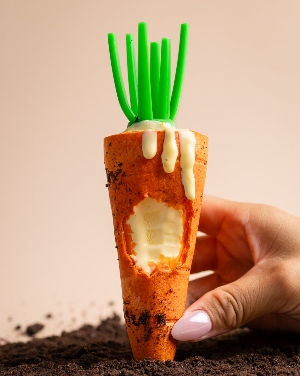 Hand holding a NiceMe carrot-shaped wafer cone with the filling visible above chocolate cookie crumbs.